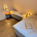 Zwei Betten mit weißen Bettwäsche und Handtüchern. Holzboden und warme Wandbeleuchtung.