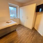 Zimmer mit Bett, Kleiderschrank und Wand-TV. Fenster mit Blick auf Dach.