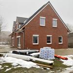 Neubauhaus mit rotem Backstein, weißen Fenstern und Dach, Baustoffe liegen im Vorgarten.