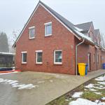 Rotes Backsteinhaus mit Schnee, Garagenbereich und Müllcontainern.