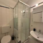 Badezimmer mit Dusche, Waschbecken und Toilette. Weiße Fliesen und Spiegelschrank.