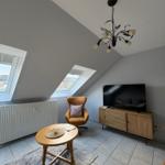 Dachgeschosswohnung mit TV, Sessel und Dachfenstern. Fliesenboden und Holzmöbel.