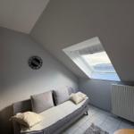 Ein Schlafzimmer mit Dachschrägen, Sofa, Fenster und Wanduhr.