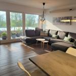 Wohnzimmer mit Ecksofa, Holzboden und Balkonansicht. Essbereich mit Tisch und Stühlen.