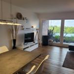 Wohn- und Essbereich mit Balkon, TV, Tisch und Stühlen sowie Pflanzen.