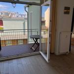 Terrasse mit Tisch und Blick auf Gebäude. Im Hintergrund ein Schlafzimmer mit Bett.