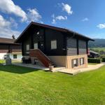 Wooden house with terrace and garden. View of green landscape and hills.