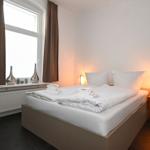 Schlafzimmer mit Bett, Nachttisch und Fenster mit Vorhängen.