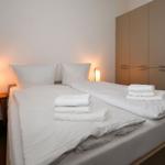 Doppelbett mit weißer Bettwäsche, zwei Nachttische mit Lampen und Kleiderschrank.