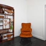 Eckzimmer mit brauner Sitzgelegenheit und Holzregal mit Dekoration. Durchgang zur Küche.