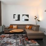 Wohnzimmer mit Ecksofa, runden Tisch und Wandbildern.