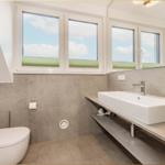 Badezimmer mit Waschtisch, Toilette und Fenstern. Holzwand und Betonfliesen.