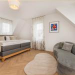 Schlafzimmer mit Doppelbett, Sessel und Holzboden. Dachschrägen und Fenster mit Vorhängen.