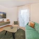 Ein Wohnzimmer mit grünem Sofa, runden Teppich und Wandbild.