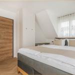 Schlafzimmer mit Doppelbett, Holztür und Fenster mit Vorhängen.