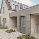 Moderne Villa mit Steinmauer, Eingangstür und gepflastertem Hof mit Blumenbeeten.