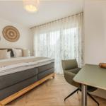 Schlafzimmer mit Doppelbett, Schreibtisch und Fenster mit Vorhängen.