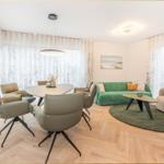 Wohn- und Essbereich mit grünem Sofa, runden Tisch und hellen Holzboden.