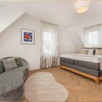 Schlafzimmer mit Doppelbett, Sofa und Holzboden. Fenster mit Vorhängen.