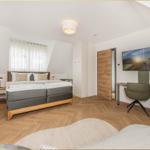 Schlafzimmer mit Doppelbett, Schreibtisch und TV. Holzboden und Dachschräge.