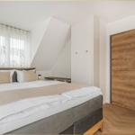 Schlafzimmer mit Doppelbett, Holztür und Fenster mit Vorhängen.