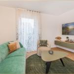 Ein Wohnzimmer mit grünem Sofa, runden Tisch und Wandbild.