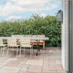 Terrasse mit Tisch, drei Stühlen und Bank. Hintergrund: grüne Hecke und Himmel.
