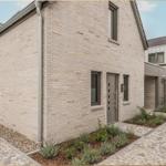 Moderne Villa mit Steinmauer und gepflastertem Hof. Eingangstür und Fenster sind sichtbar.