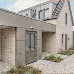 Moderne Villa mit Steinmauer, Glasfront und gepflastertem Hof. Eingangstür und Gartenbereich sichtbar.