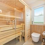 Sauna mit Holzbank und Eingangstür. Neben dem WC befindet sich ein Fenster.