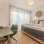 Schlafzimmer mit Bett, Schreibtisch und TV. Holzfußboden und weiße Wände.