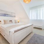 Schlafzimmer mit Doppelbett, Fenster, Nachttische und Wandbildern.