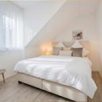 Schlafzimmer mit Dachschräge, Bett, Fenster und Wandbild.