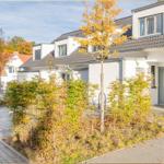 Moderne weiße Wohnhäuser mit grauem Dach und Bäumen im Herbst.