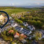 Luftbild eines Dorfes mit Häusern, Wiesen und einem See im Hintergrund.