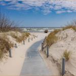 Holzweg durch Sanddünen zur See mit Fischerboot.