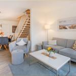 Wohn- und Essbereich mit Sofa, Sessel und Treppe. Wandbild zeigt Strand.