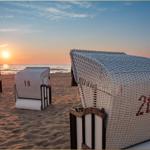 Drei weiße Strandkörbe mit Nummern stehen am Strand bei Sonnenuntergang.