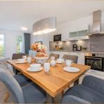 Essbereich mit Holztisch und Stühlen. Küche mit weißen Schränken und Edelstahlgeräten.