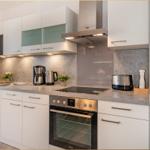 Küche mit weißen Schränken, Edelstahlgeräten und grauer Arbeitsplatte.