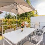 Terrasse mit Tisch, Stühlen und Sonnenschirm. Hintergrund: Bäume und ein weißer Zaun.