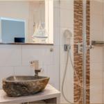 Bad mit Steinwaschbecken, Dusche und Spiegel. Wandverkleidung aus Steinfliesen.