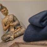 Buddha-Figur auf Steinbank neben blauem Kissen