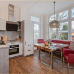 Küche und Essbereich mit rotem Sofa, Glas-Tisch und großen Fenstern.