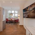 Wohnbereich mit Essbereich, roten Sitzgelegenheiten und Wandbild. Holzboden und große Fenster.