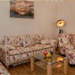 Wohnzimmer mit floralen Sitzmöbeln, Glas-Tisch und Wandbild.