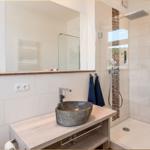 Bad mit Dusche, Steinwaschbecken und Spiegelschrank. Handtuchhalter und Steckdosen sind vorhanden.