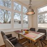 Esszimmer mit Glas-Tisch, Stühlen und großen Fenstern. Draußen sind Bäume und Häuser sichtbar.