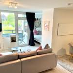 Wohnbereich mit Sofa, TV und Balkonzugang. Schlafzimmer im Hintergrund.