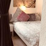 Schlafzimmer mit Bett, Kissen und Wandbild. Dunkle Vorhänge und Licht an der Wand.